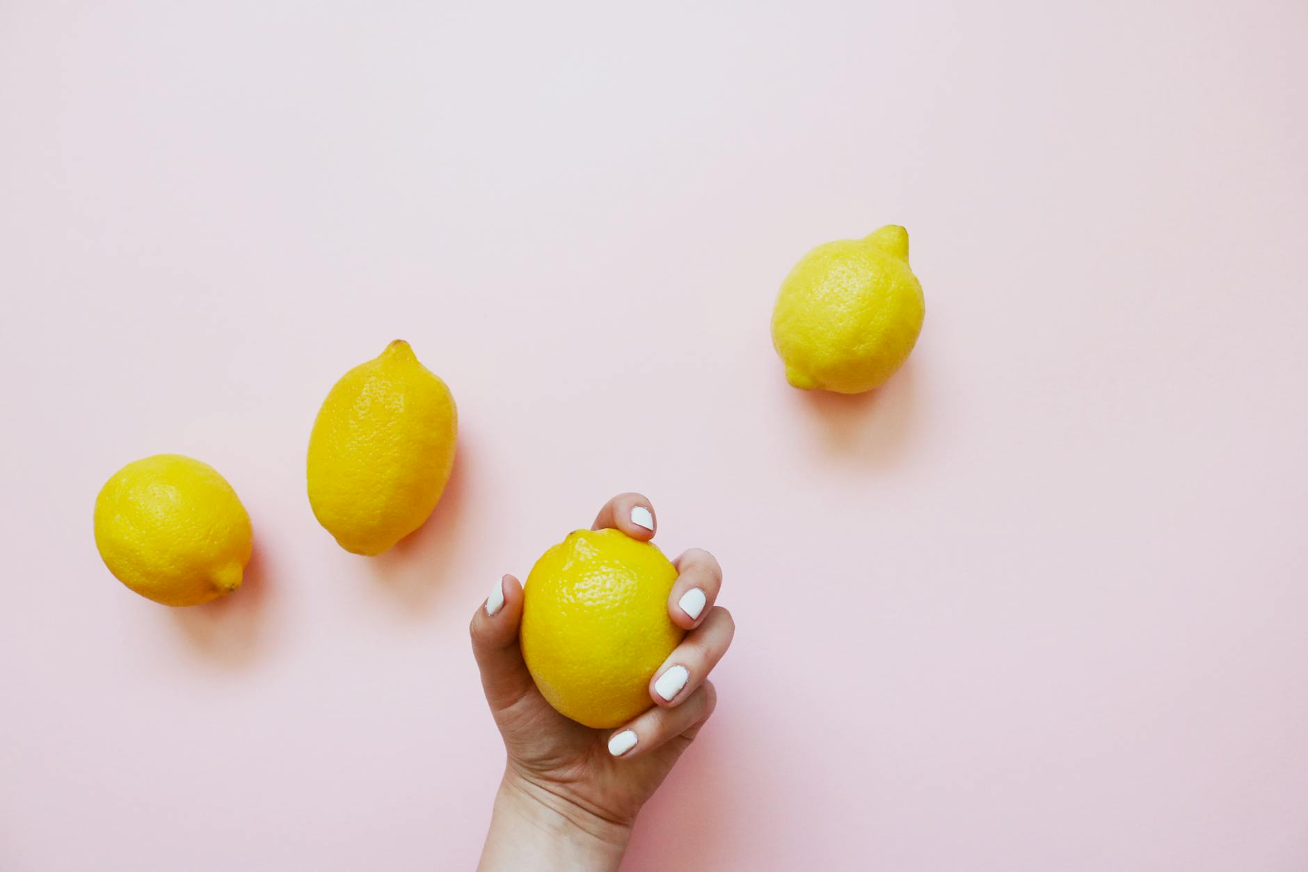 Hand holding a lemon on a soft pink background, symbolizing freshness and renewed sensation