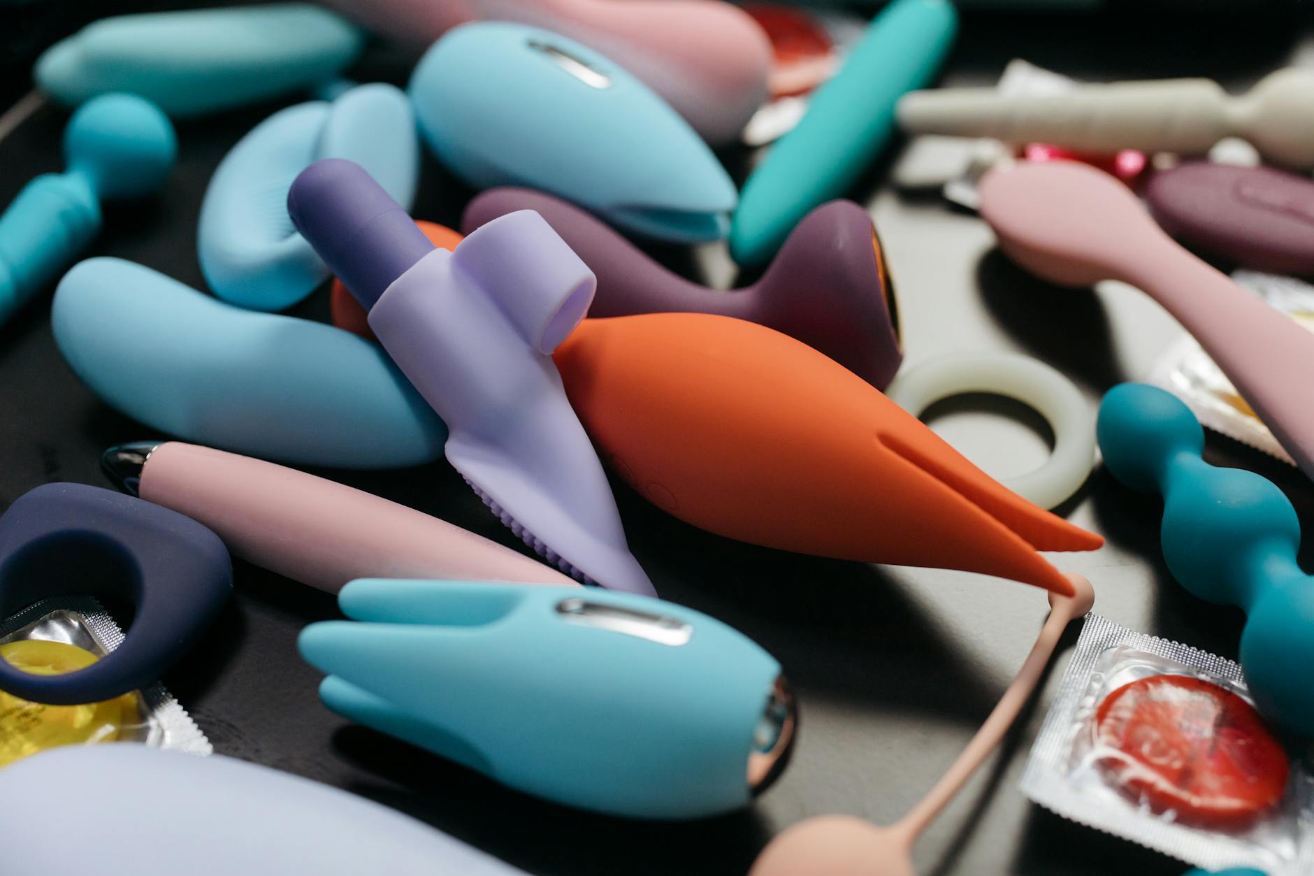 Woman with eyeglasses holding blue and pink silicone vibrators in a contemplative manner