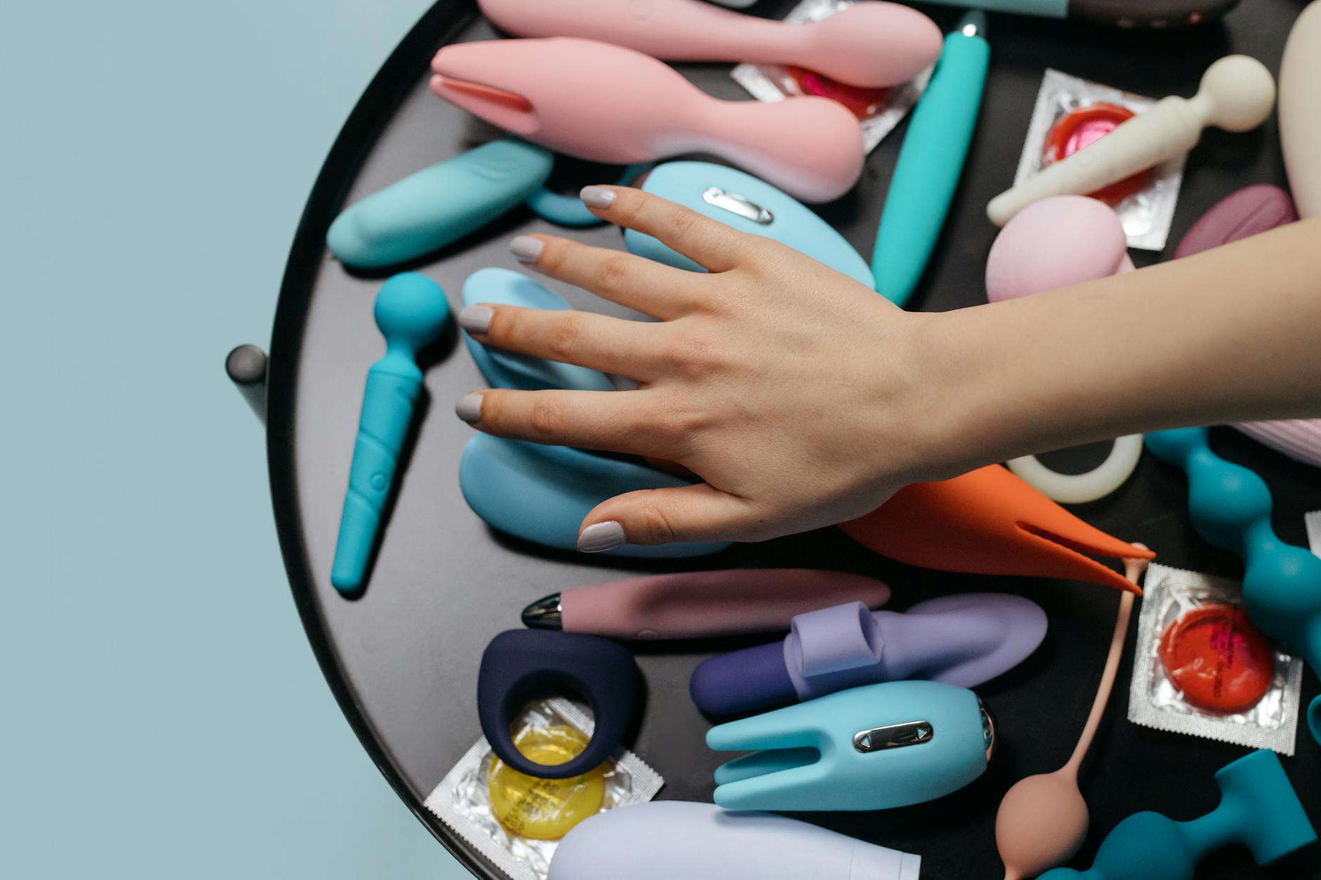 Hand reaching over a variety of colorful clitoral vibrators arranged on a table