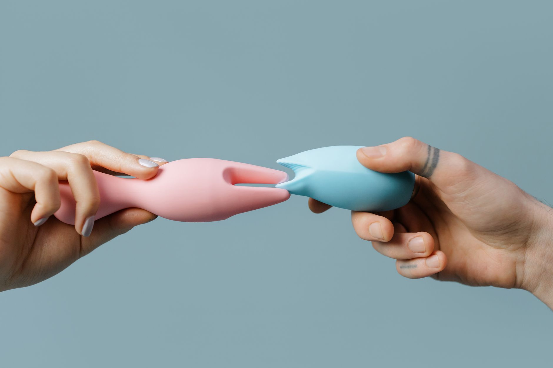 Woman holding blue and pink silicone vibrators thoughtfully