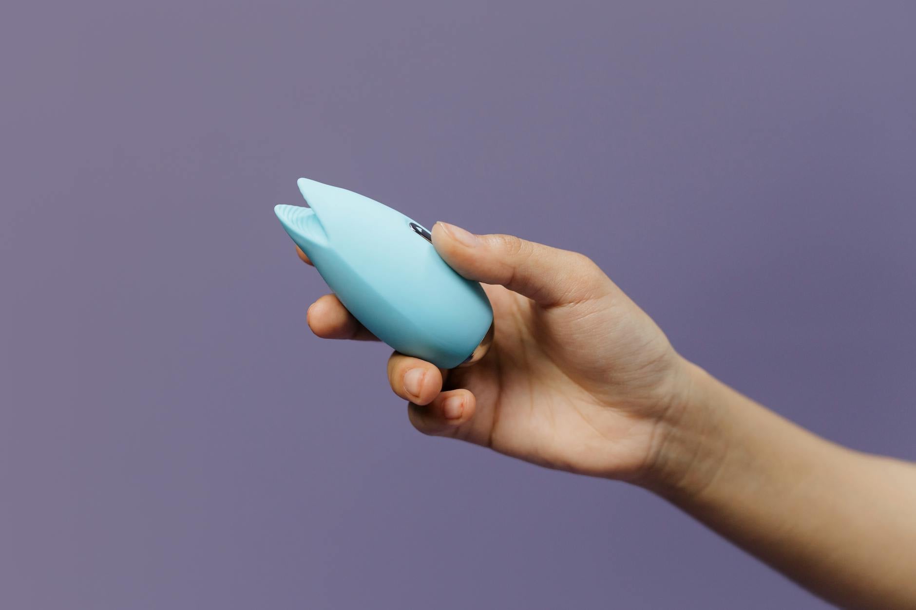 Blue silicone lemon vibrator held in hand against purple background