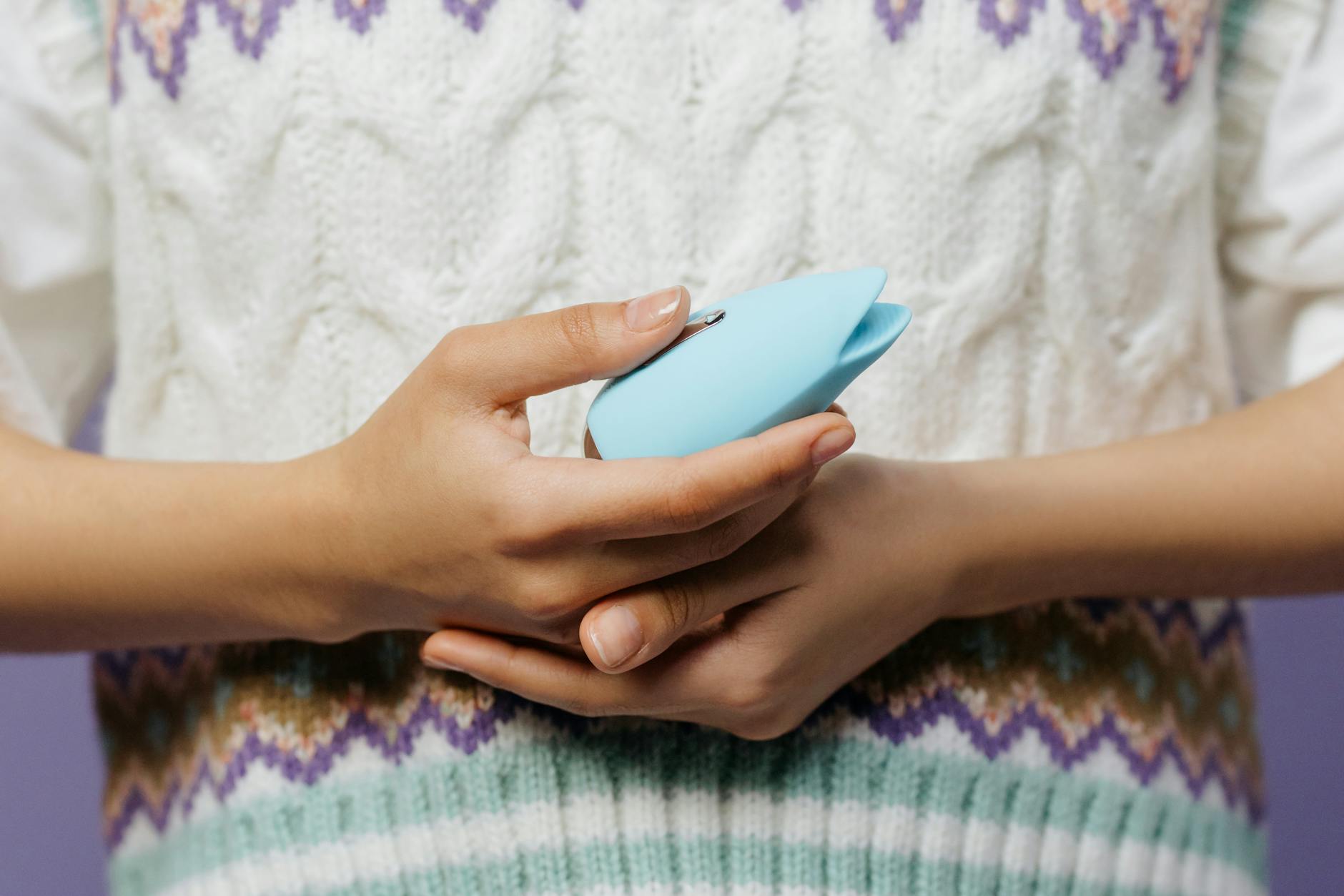 Two hands holding pink and blue silicone vibrators against a pastel background, representing couple's intimacy