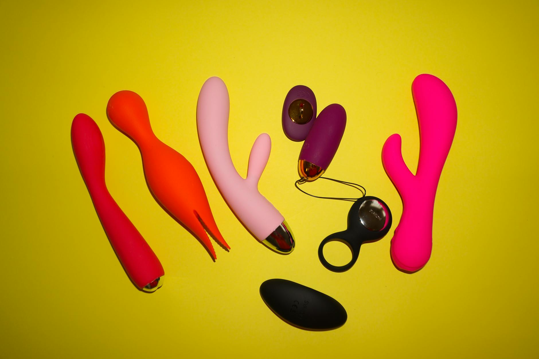Woman thoughtfully holding blue and pink silicone vibrators against solid background